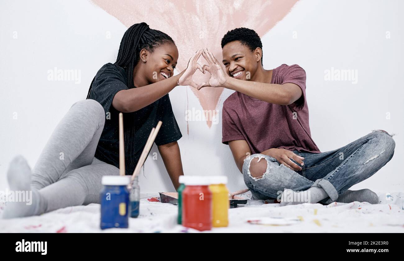 Suivez votre cœur et vous trouverez chez vous. Photo d'un jeune couple faisant un geste en forme de coeur tout en peignant un mur rose. Banque D'Images