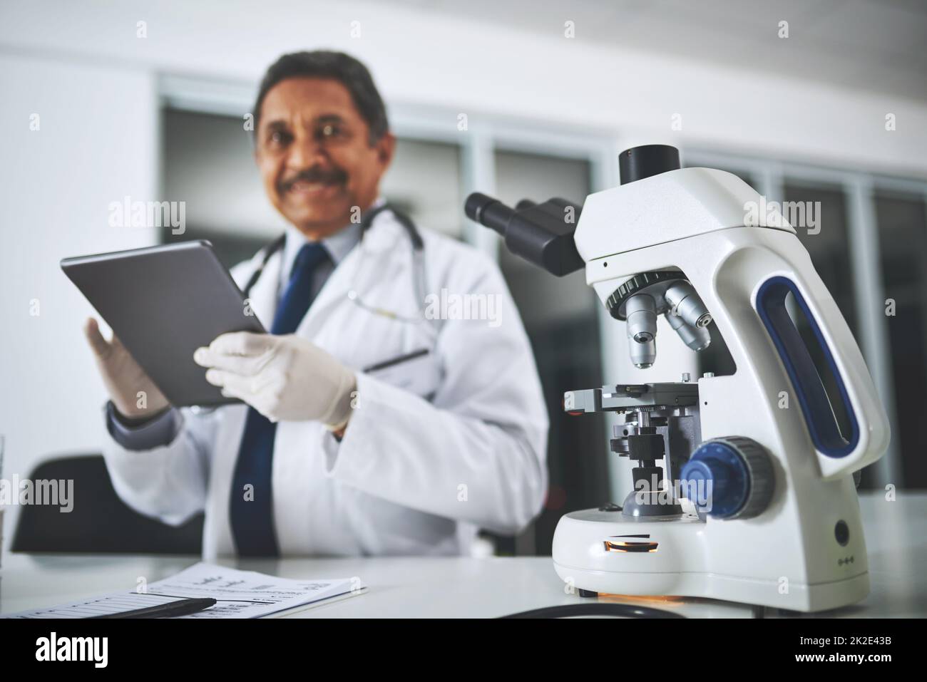 La recherche médicale qui fait la différence. Cliché d'un microscope sur une table de laboratoire avec un scientifique utilisant une tablette numérique en arrière-plan. Banque D'Images