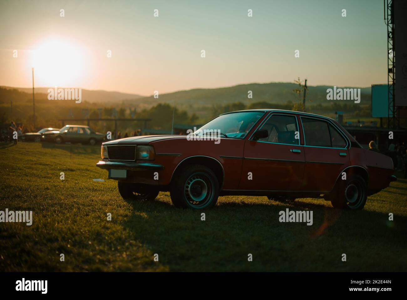 La voiture rouge vintage reste sur l'herbe au coucher du soleil Banque D'Images