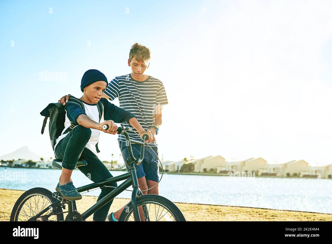 Enseigner à son frère comment faire un vélo. Plan court d'un jeune garçon expliquant à son frère cadet comment faire un vélo le long d'un lagon. Banque D'Images