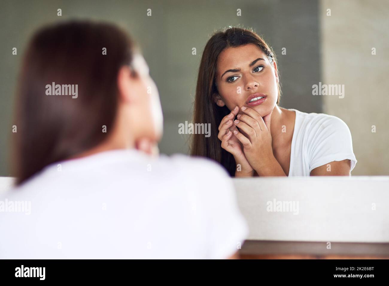 D'où vient cette situation. Prise de vue d'une jeune femme qui se froisait et qui examine une imperfection sur sa peau dans le miroir à la maison. Banque D'Images