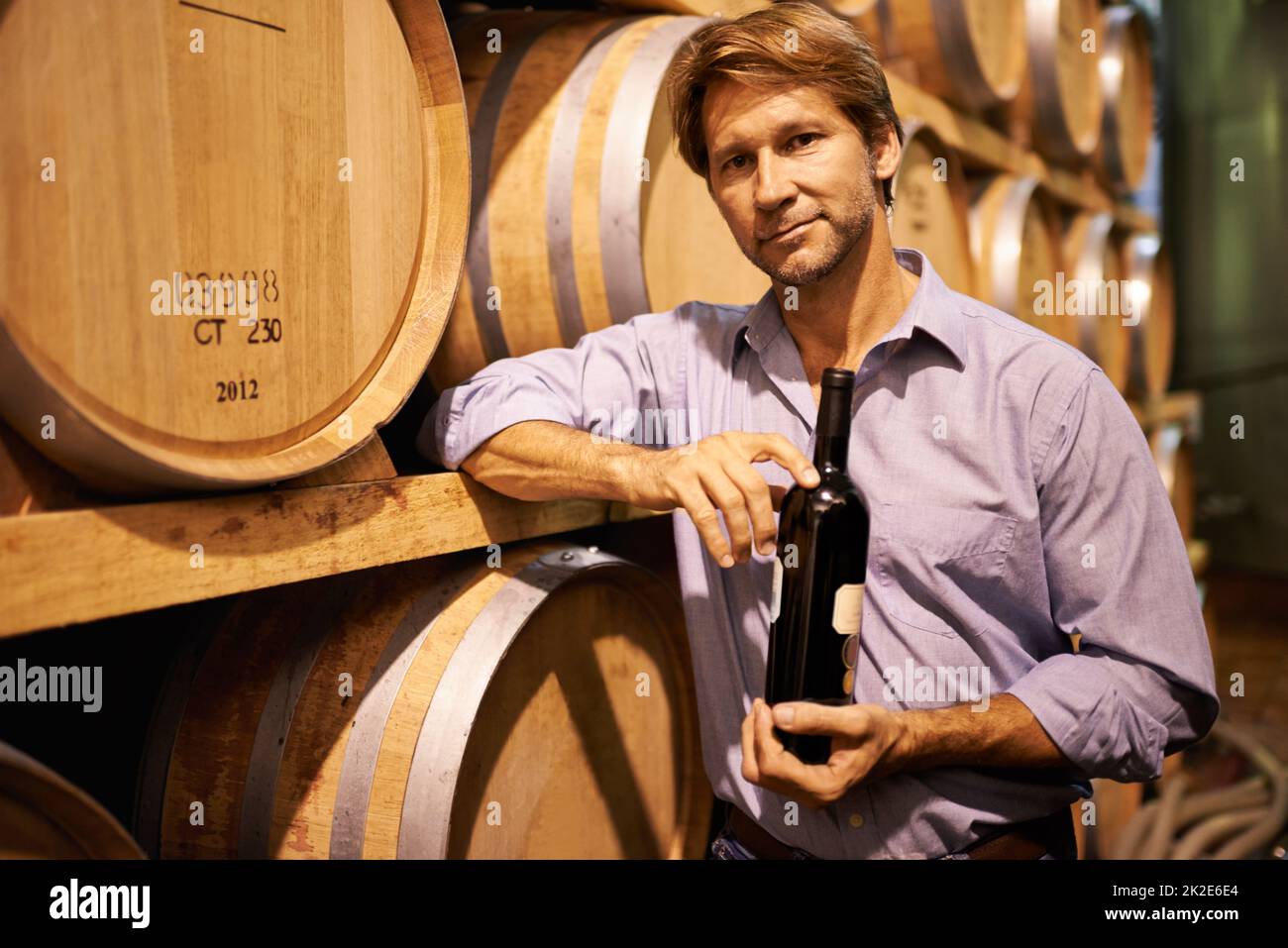 Le bon vin pour chaque occasion. Portrait d'un beau homme mûr debout dans une cave à vin avec une bouteille de vin. Banque D'Images