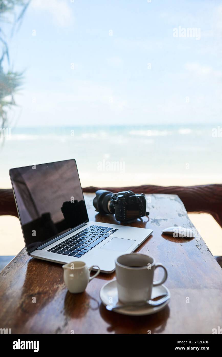Blogging à la plage. Photo d'un ordinateur portable et d'une tasse de café sur une table avec vue sur la plage en arrière-plan. Banque D'Images