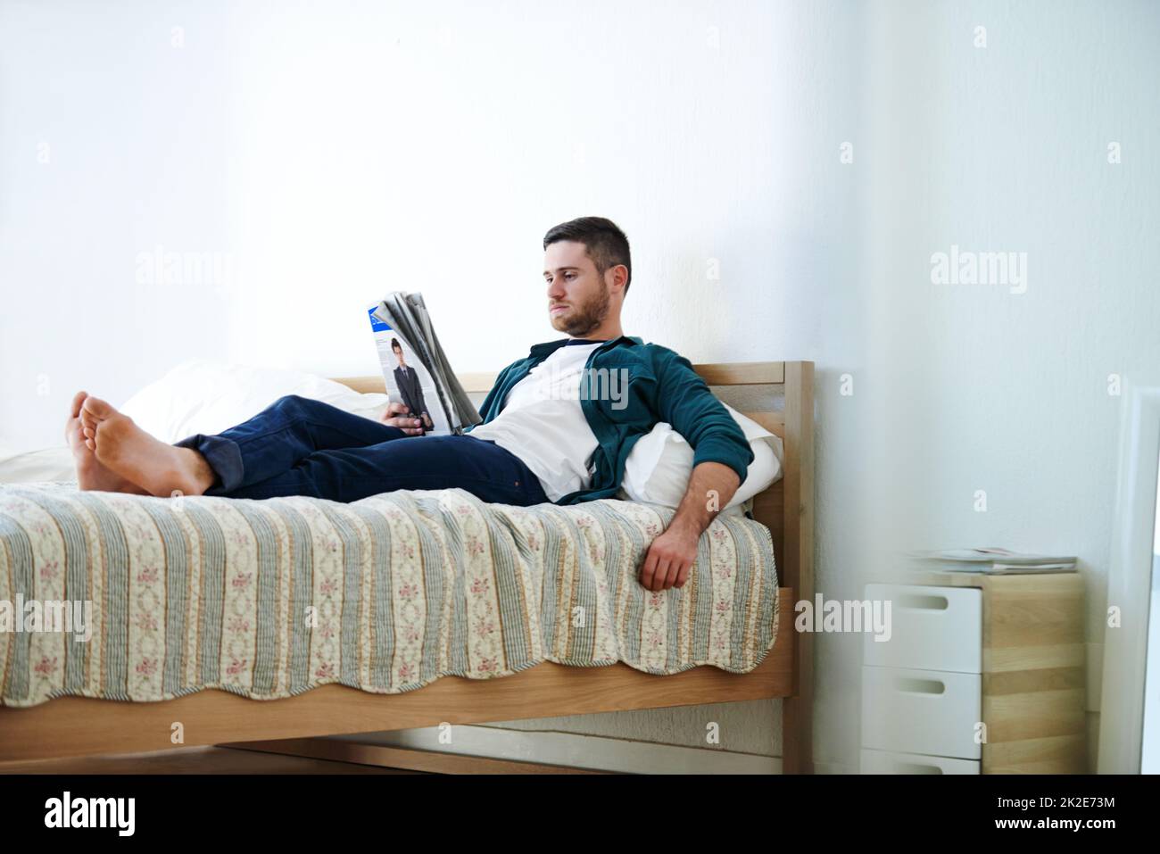 Un peu de rattrapage. Photo d'un beau jeune homme allongé sur son lit en lisant un magazine. Banque D'Images