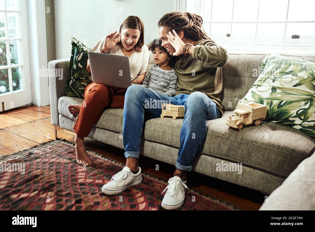 Faites un mouvement vers la caméra. Photo d'un jeune couple joyeux et de son fils ayant un appel vidéo à des parents sur un ordinateur portable tout en étant assis sur un canapé à la maison. Banque D'Images