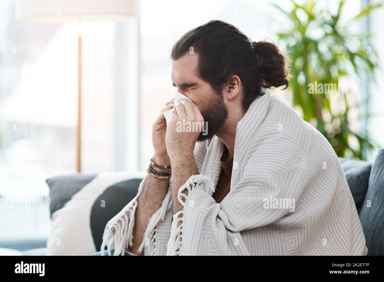 C'est le pire moment pour être malade. Photo d'un jeune homme malade soufflant son nez avec un tissu dans son salon. Banque D'Images