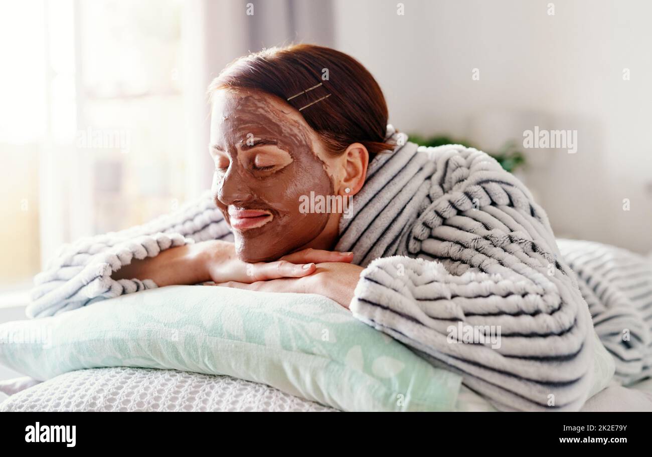 Je me sens déjà très bien. Plan court d'une jeune femme attrayante couché sur son lit avec un masque de boue sur son visage le matin à la maison. Banque D'Images