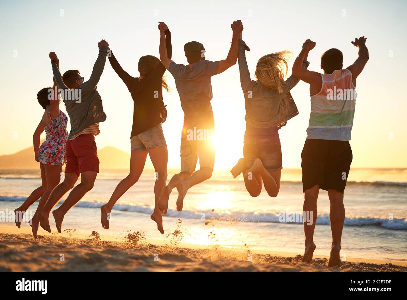 United We voler. Vue arrière d'un groupe de jeunes amis qui sautent dans les airs tout en tenant les mains à la plage. Banque D'Images