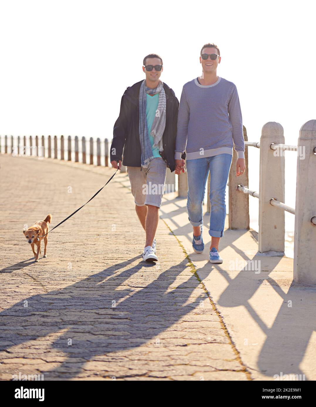 Promenade en bord de mer avec notre petite princesse. Photo d'un jeune couple gay en train de se promener sur la promenade avec son chien. Banque D'Images