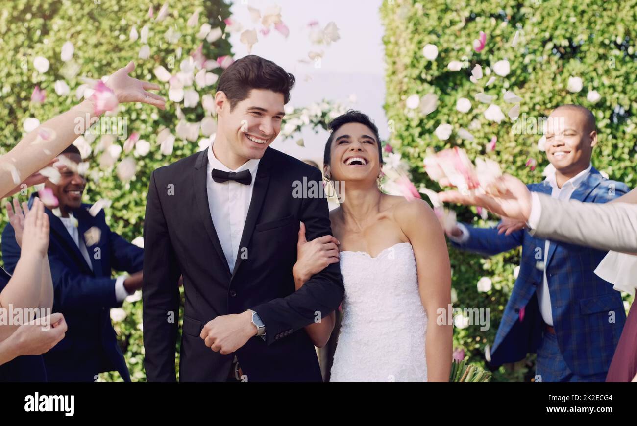 Et ils sont heureux à la fin Prise de vue courte d'un jeune couple affectueux et nouveau-né quittant leur lieu de mariage avec leurs invités jetant des confettis en arrière-plan. Banque D'Images