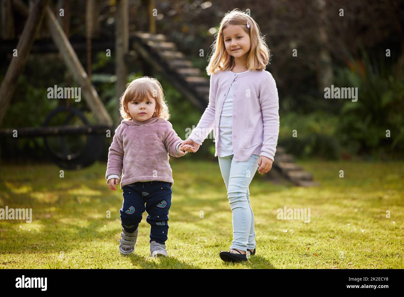 Shes va grandir pour être mon meilleur ami. Portrait complet de deux adorables petites sœurs debout main dans la main dans le jardin à la maison. Banque D'Images