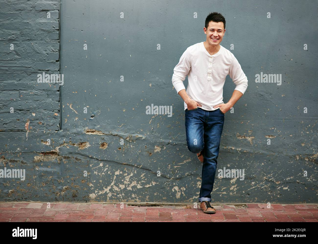 HES un homme facile à utiliser. Portrait d'un beau jeune homme debout avec ses mains dans ses poches contre un mur gris. Banque D'Images