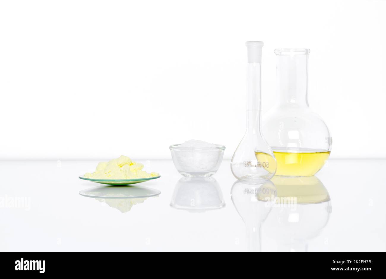 Poudre de soufre dans le verre de surveillance chimique placer à côté du produit chimique en flocons blancs dans un récipient en verre, dans une fiole jaugée et dans un liquide de chlorure d'aluminium dans un flacon à fond plat. Vue latérale Banque D'Images