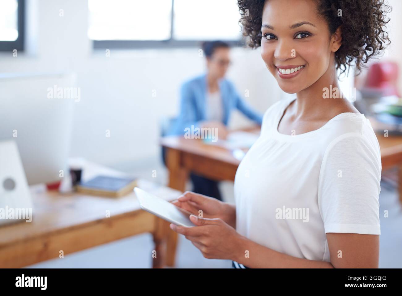 J'adore la commodité de la technologie moderne. Belle femme d'affaires souriant à la caméra avec un espace de bureau ouvert derrière elle. Banque D'Images