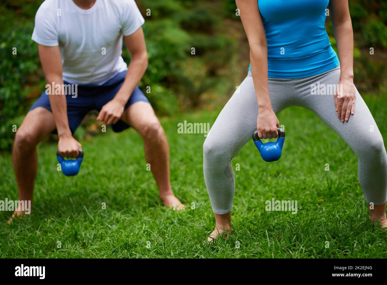 Travailler ces muscles. Coupe courte d'un homme et d'une femme utilisant des poids de cloche de bouilloire lors d'un cours d'exercice en plein air. Banque D'Images