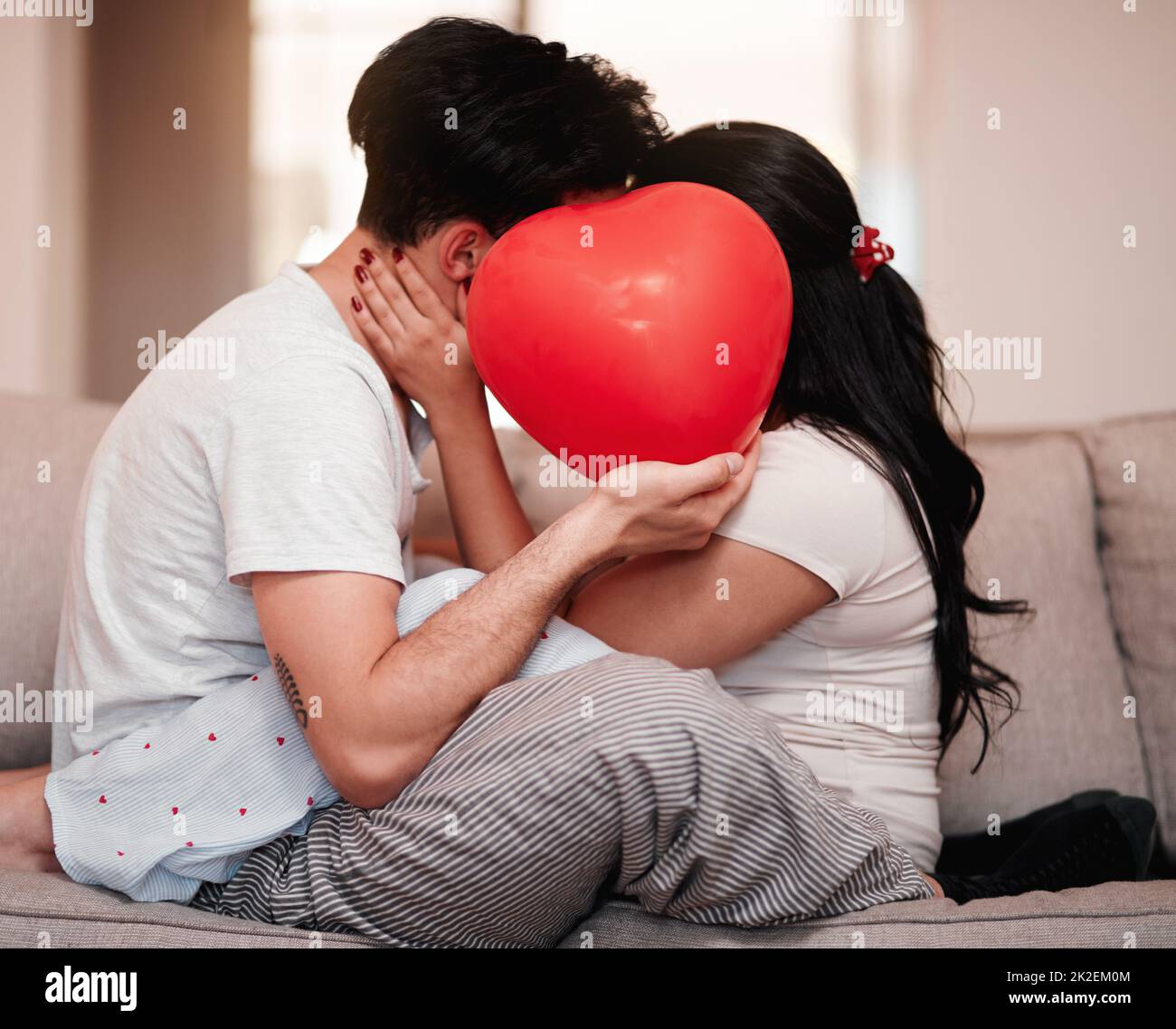 L'amour est la raison. Photo courte d'un jeune couple méconnaissable embrassant derrière un ballon en forme de cœur le jour de la Saint-Valentin. Banque D'Images