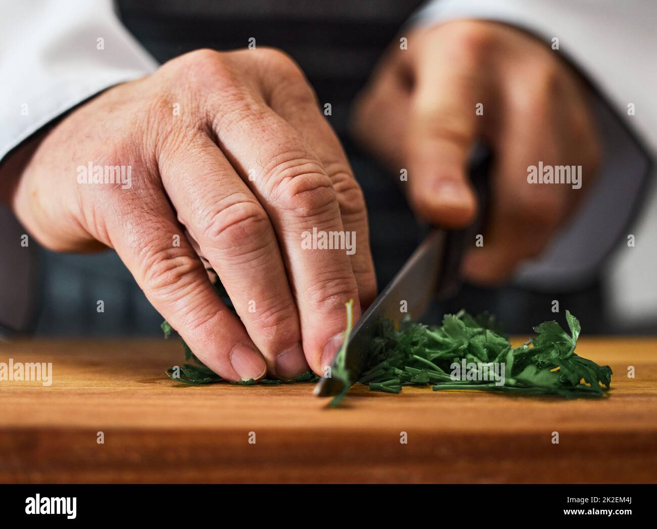 Herbes, les héros méconnus de toute histoire culinaire. Photo d'un homme méconnu qui coupe du persil frais sur une planche à découper. Banque D'Images
