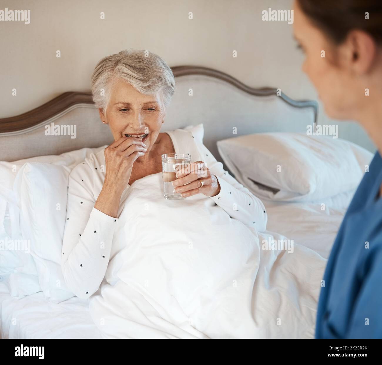Vitamines pour que la vitalité boost. Prise d'une infirmière donnant à une femme âgée son médicament à prendre avec un verre d'eau au lit. Banque D'Images