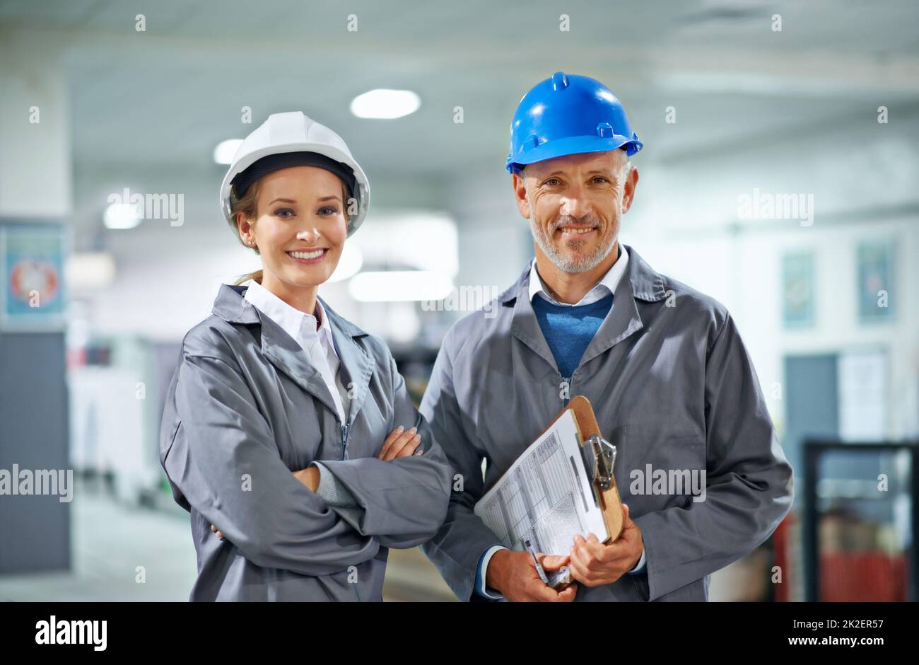 Heureux dans notre profession. Deux personnes portant des casques de sécurité souriant à la caméra dans une usine. Banque D'Images