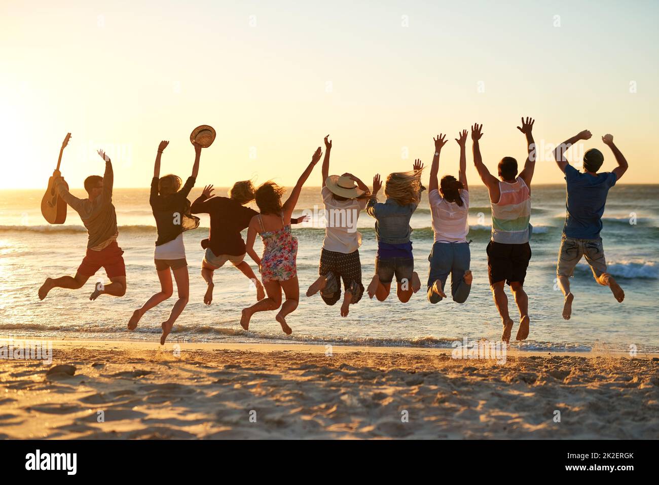 C'est le meilleur été jamais vu. Vue arrière d'un groupe de jeunes amis qui sautent dans les airs à la plage. Banque D'Images