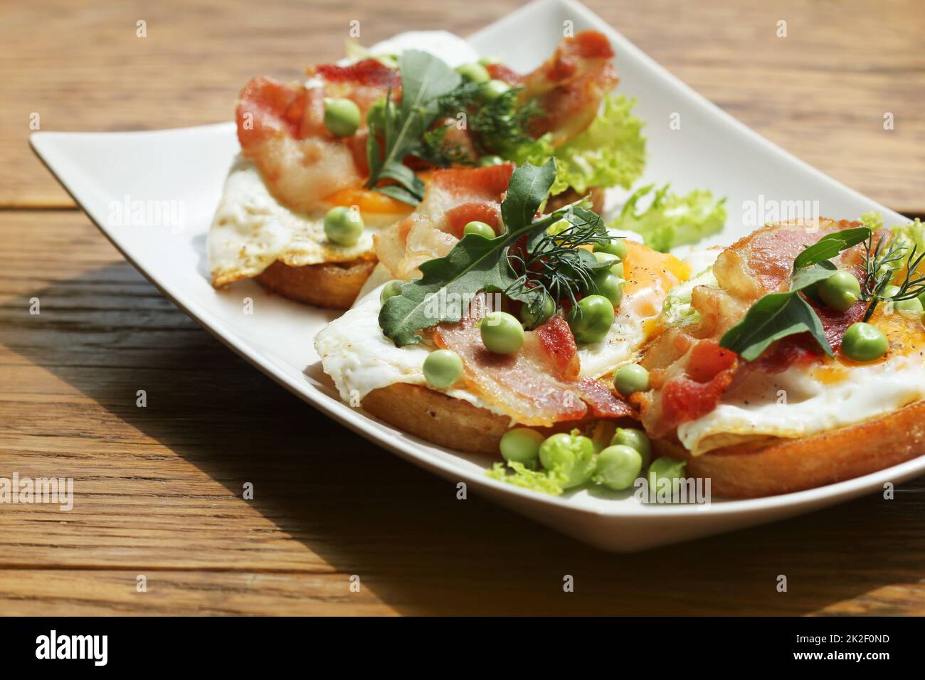 Bruschetta avec rucola, chrispy bacon et œuf poché servi sur plaque blanche Banque D'Images