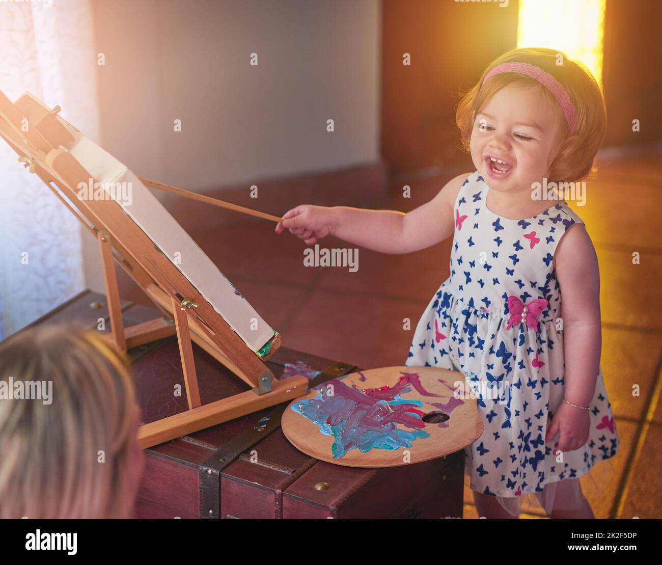 Chef-d'œuvre en cours. Photo d'une adorable petite fille peignant une photo tandis que sa mère regarde à la maison. Banque D'Images