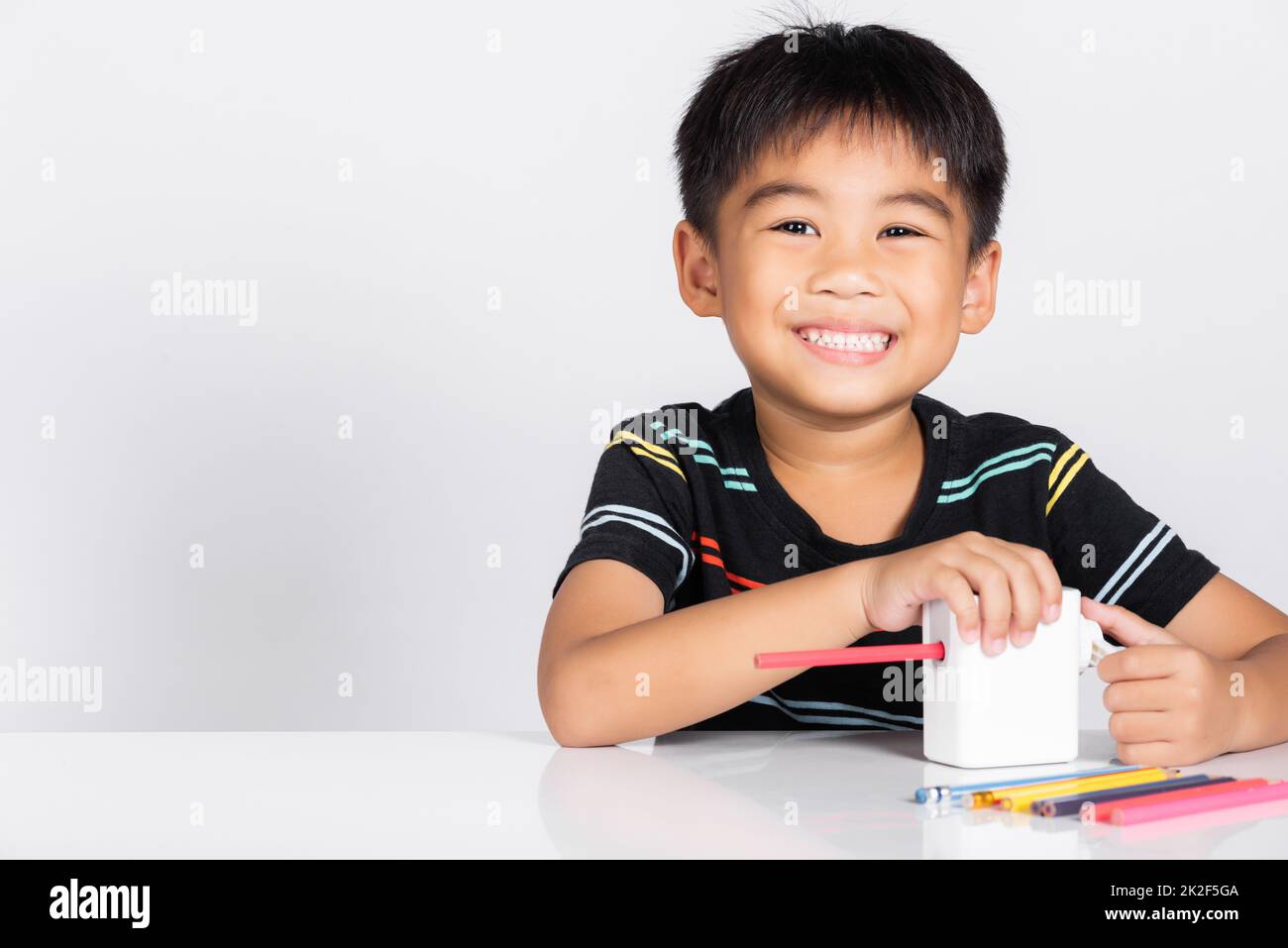 Un petit garçon mignon de 5-6 ans sourira en utilisant un taille-crayon tout en faisant vos devoirs Banque D'Images