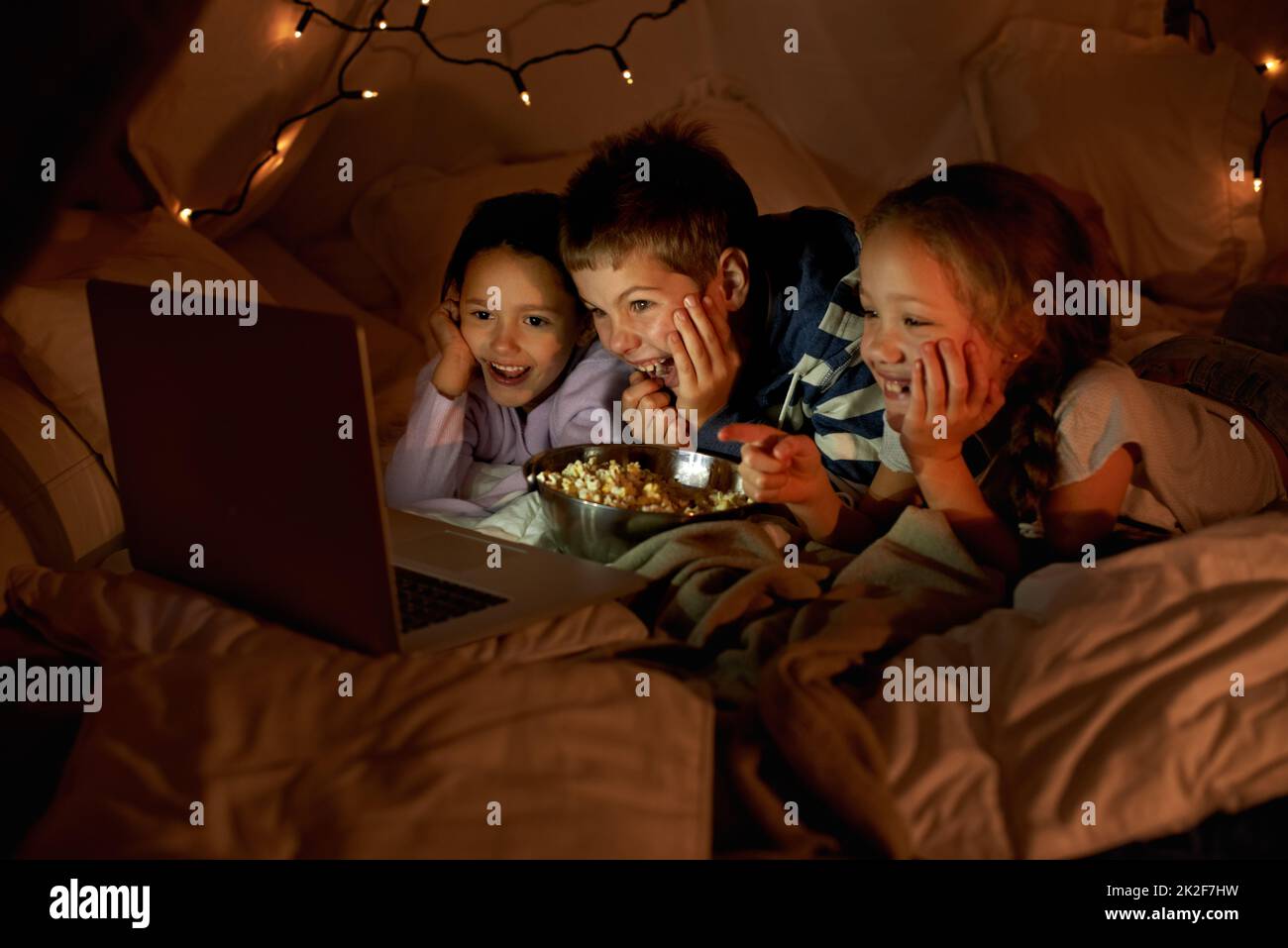 Les enfants ne sont jamais loin de la technologie. Photo de trois jeunes enfants utilisant un ordinateur portable dans un fort de couverture. Banque D'Images