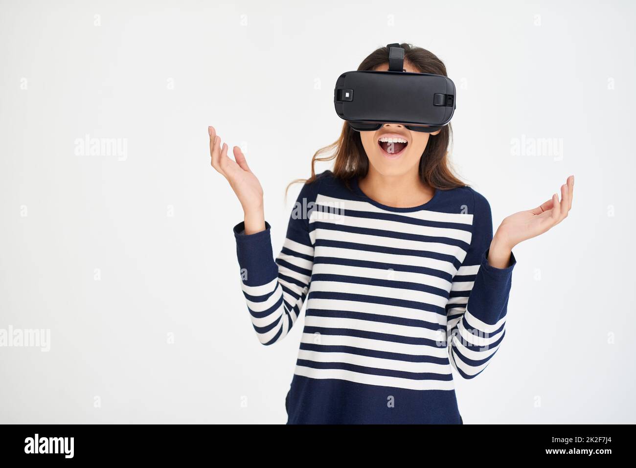 C'est tellement irréel. Photo en studio d'une jeune femme qui a l'air stupéfait en portant un casque VR sur fond blanc. Banque D'Images