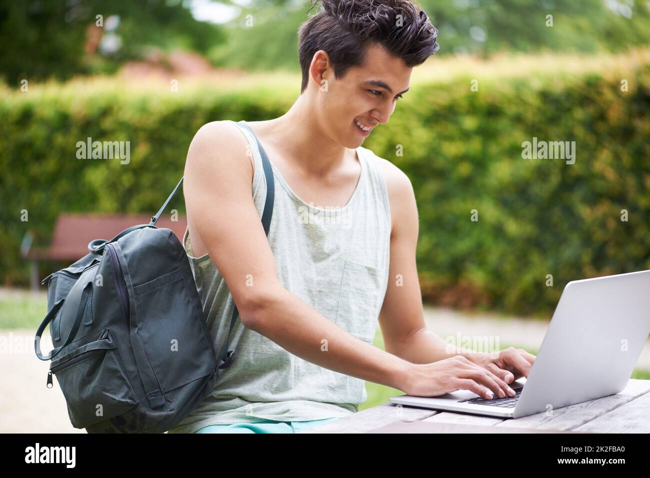 Mise en réseau n'importe où et n'importe quand. Un beau jeune homme qui tape sur son ordinateur portable tout en étant assis dans le parc. Banque D'Images