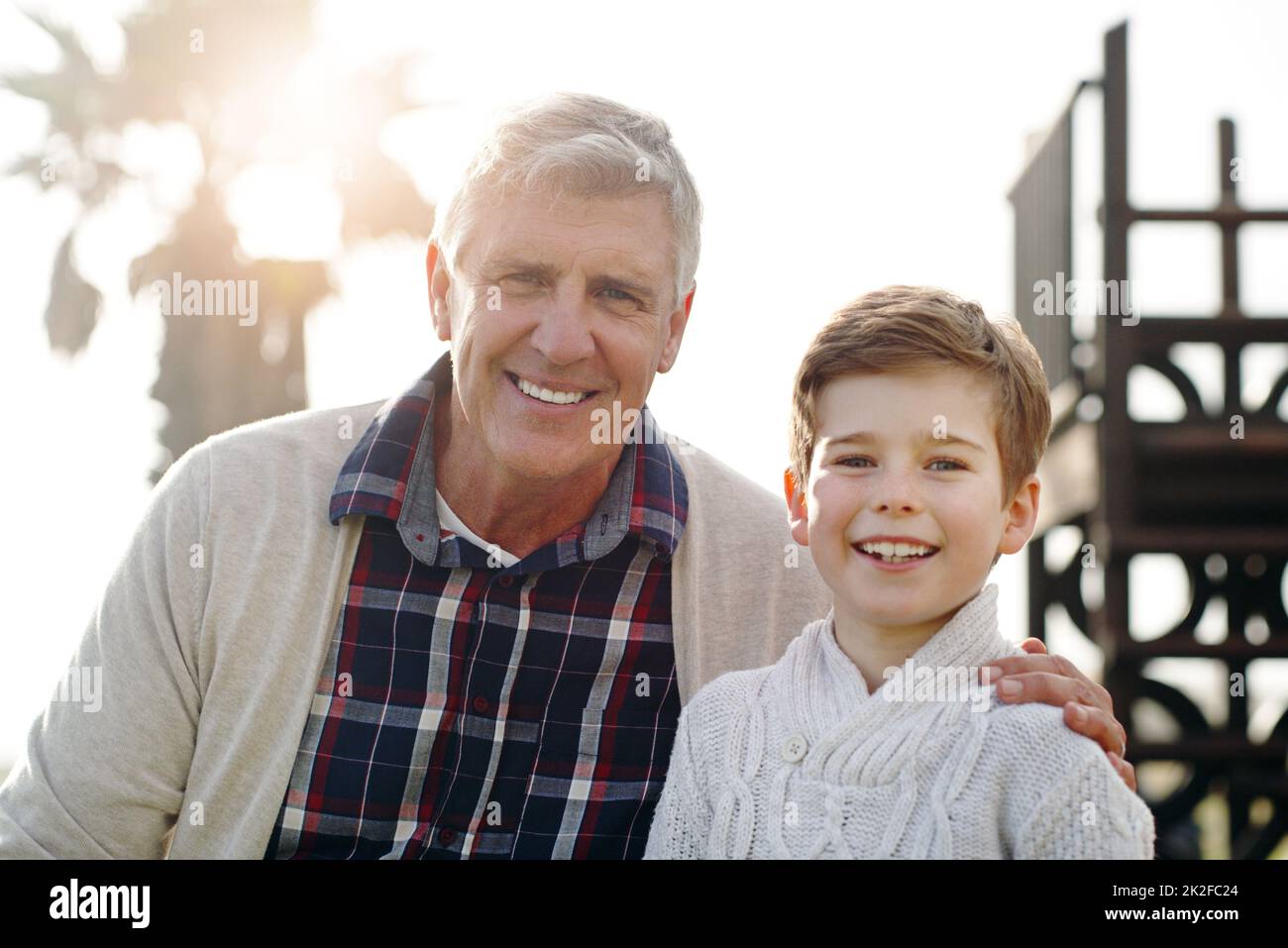 Il est sûr de dire que le système IVE a transmis les bons gènes. Portrait d'un adorable petit garçon posant avec son grand-père tout en se relaxant à l'extérieur. Banque D'Images