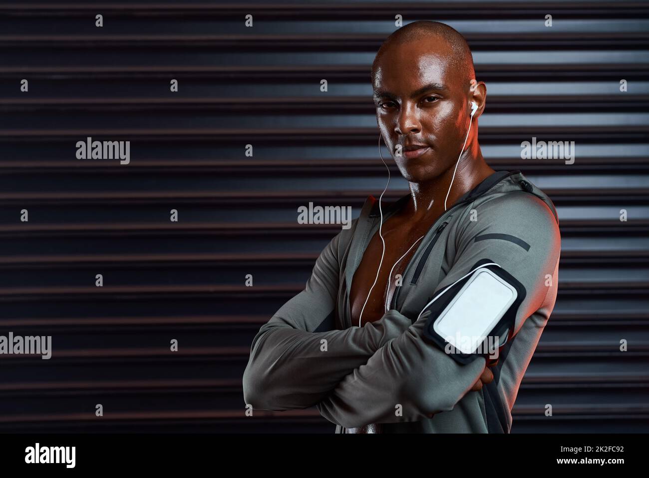 Nous ne jouons pas ici. Photo studio d'un jeune homme sportif posant avec ses bras pliés tout en écoutant de la musique sur fond gris. Banque D'Images