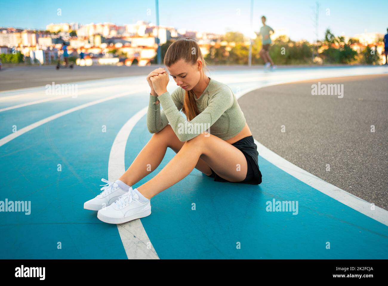 Athlète féminine fatiguée et bouleversée assise sur une piste de course à pied après des exercices de jogging. Résultat sportif déçu. Sprinter amateur sportswoman épuisé après des entraînements difficiles assis sur la piste Banque D'Images