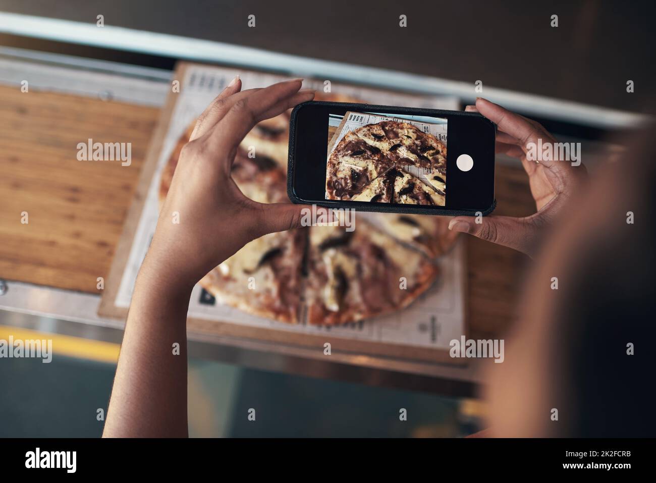 Je dois mettre ceci sur mon blog. Photo rognée d'une femme méconnue assise seule et utilisant son téléphone portable pour photographier sa pizza dans un restaurant. Banque D'Images