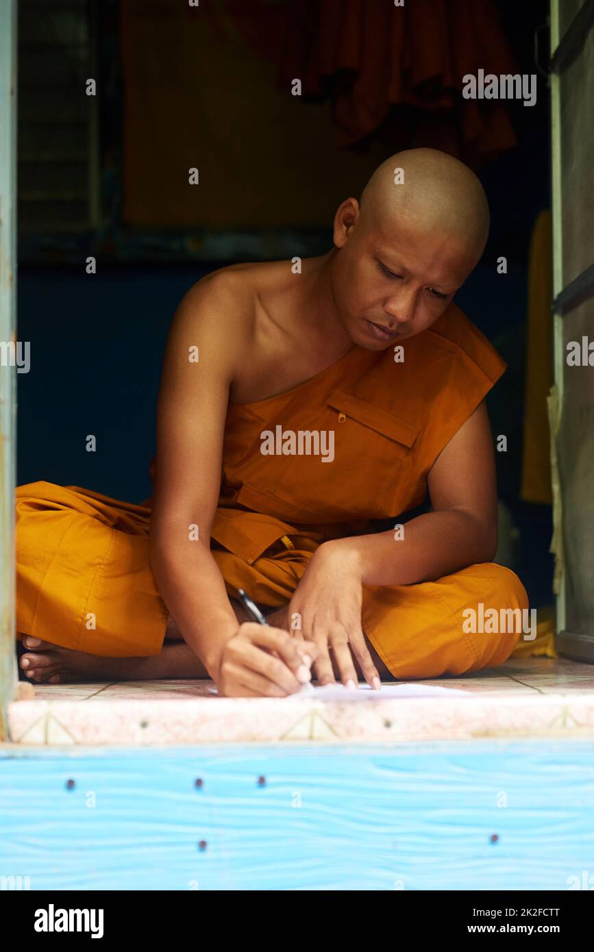 Nous nous pensions profondément. Photo d'un moine bouddhiste remplissant une forme tout en étant assis dans la porte de sa maison. Banque D'Images