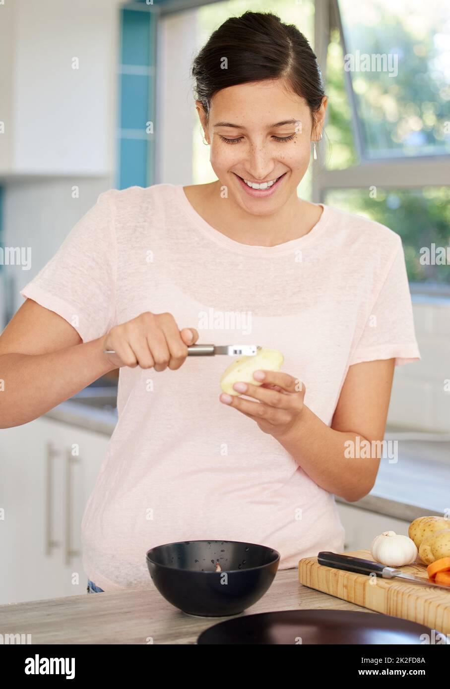 Je ne veux pas voir de skins. Photo d'une jeune femme qui éplucher une pomme de terre dans sa cuisine. Banque D'Images