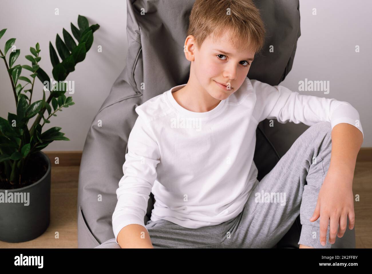 Décontracté et élégant adolescent assis sur un fauteuil à sac de haricots à la maison. Maquette de t-shirt blanche Banque D'Images