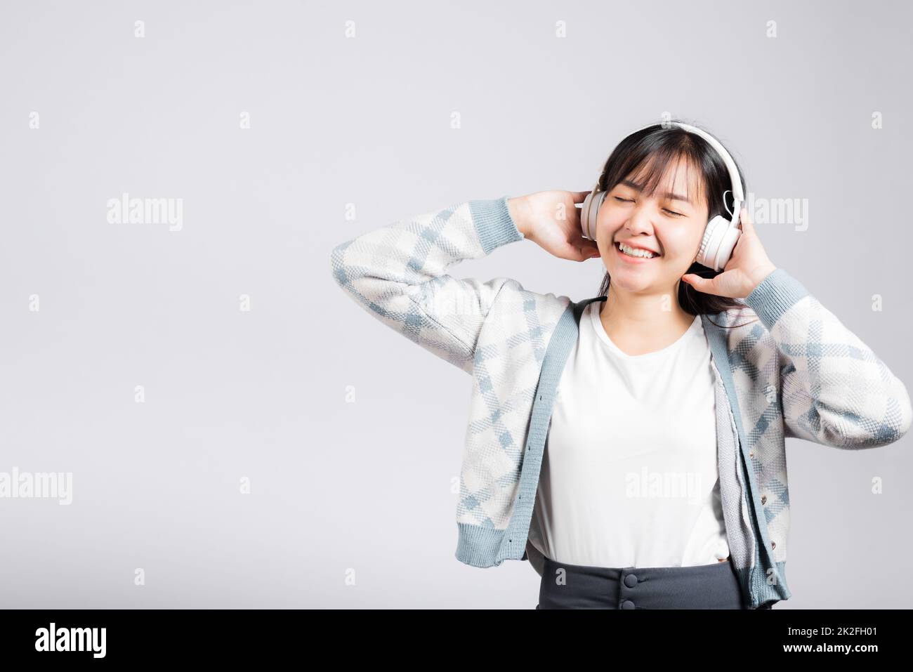 Une femme se réjouit de sourire en écoutant de la radio musicale dans un casque bluetooth et en tenant le téléphone Banque D'Images