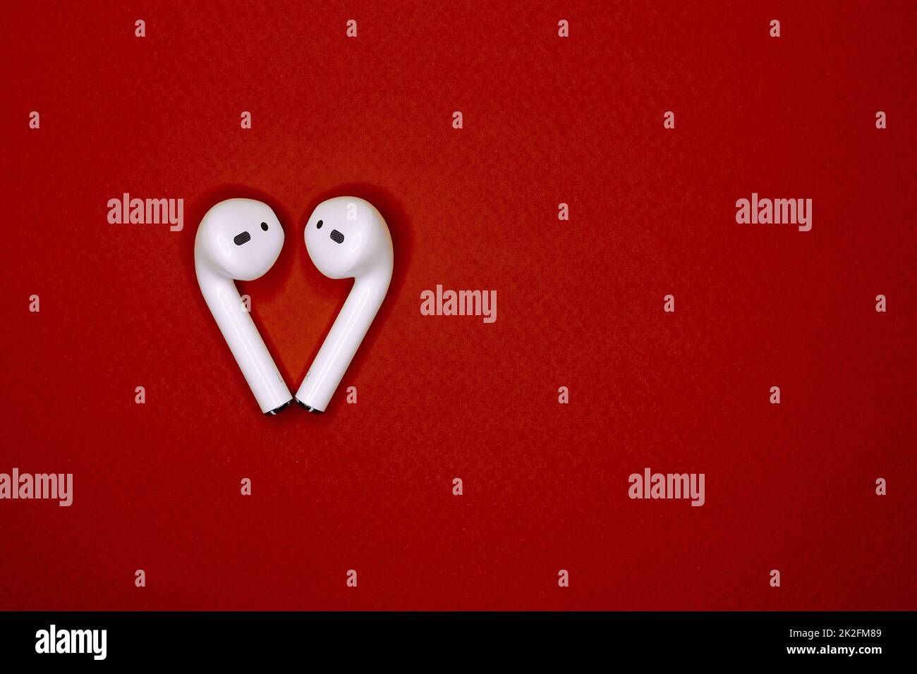 les casques sans fil blancs sont situés sur un arrière-plan rouge isolé sous la forme d'une vue du dessus du cœur. concept de communication, technologie, amour. espace pour le texte. journée internationale de la musique du monde et de la saint-valentin Banque D'Images