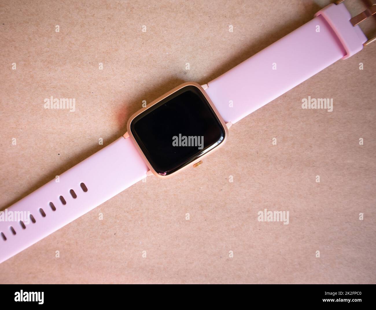 Montre intelligente sans fil avec bracelet rose isolée sur fond de papier kraft brun Banque D'Images