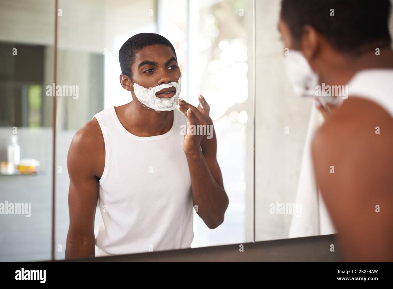 Se débarrasser des poils tenaces. Un jeune homme se raser dans le miroir. Banque D'Images