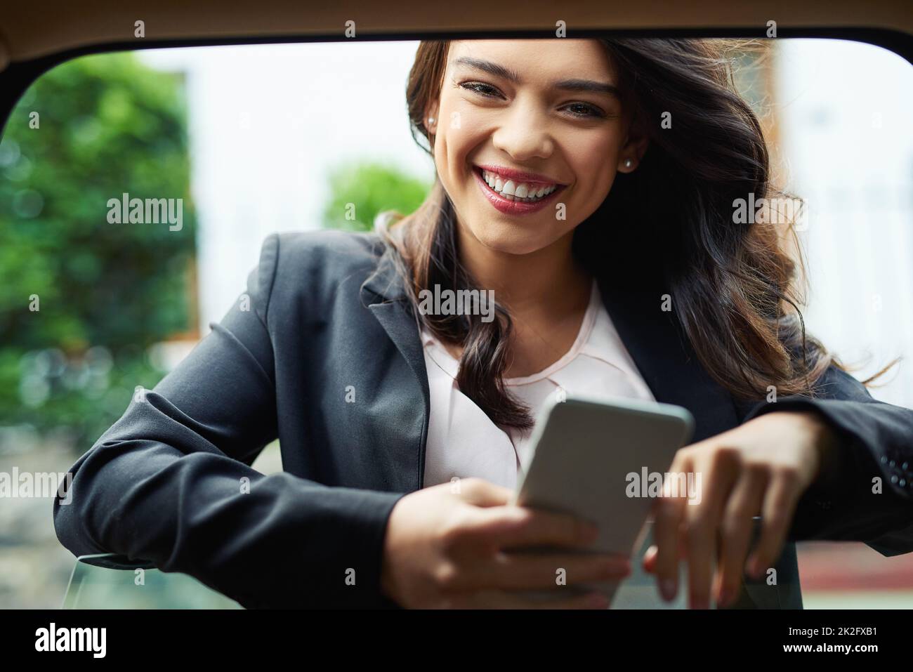 Je planifie toujours ma journée avant d'y aller. Photo d'une jeune femme d'affaires attirante utilisant un téléphone portable appuyé sur la fenêtre d'une voiture. Banque D'Images