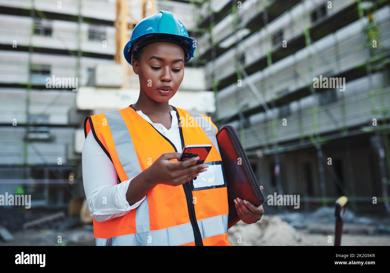 Oubliez le bureau, utilisez votre téléphone. Photo d'une jeune femme utilisant un smartphone tout en travaillant sur un chantier de construction. Banque D'Images