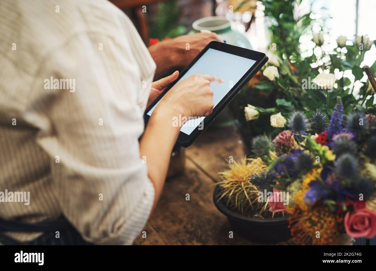 Cette application m'aide à garder une trace de tous mes stocks. Plan rogné d'un fleuriste méconnaissable à l'aide d'une tablette numérique tout en travaillant à l'intérieur de sa pépinière. Banque D'Images