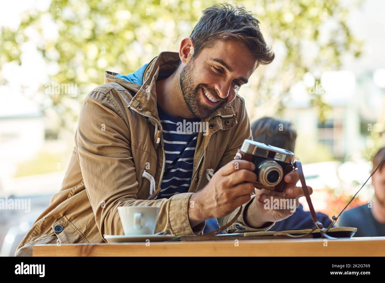 Ces clichés illustrent mon parcours. Photo d'un touriste heureux prenant une photo avec son appareil photo tout en se relaxant dans un café-terrasse. Banque D'Images