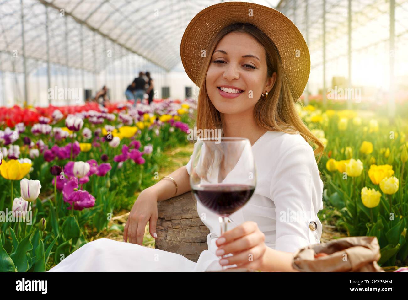 Belle femme détendue appréciant un verre de vin rouge entre tulipes au printemps Banque D'Images