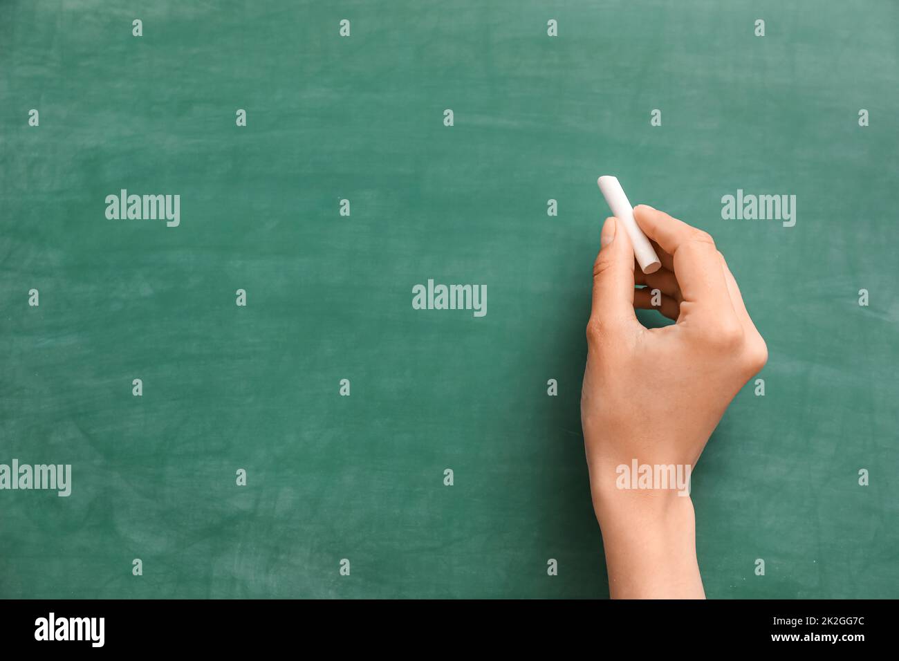 Female hand with chalk against green blackboard Banque D'Images