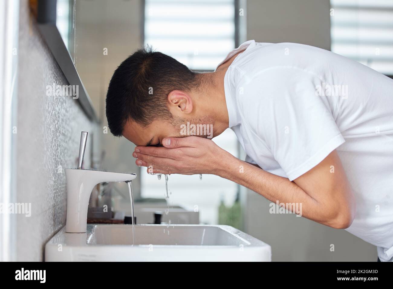 L'eau est parfaite pour votre peau. Photo d'un jeune homme lavant son visage dans une salle de bains à la maison. Banque D'Images