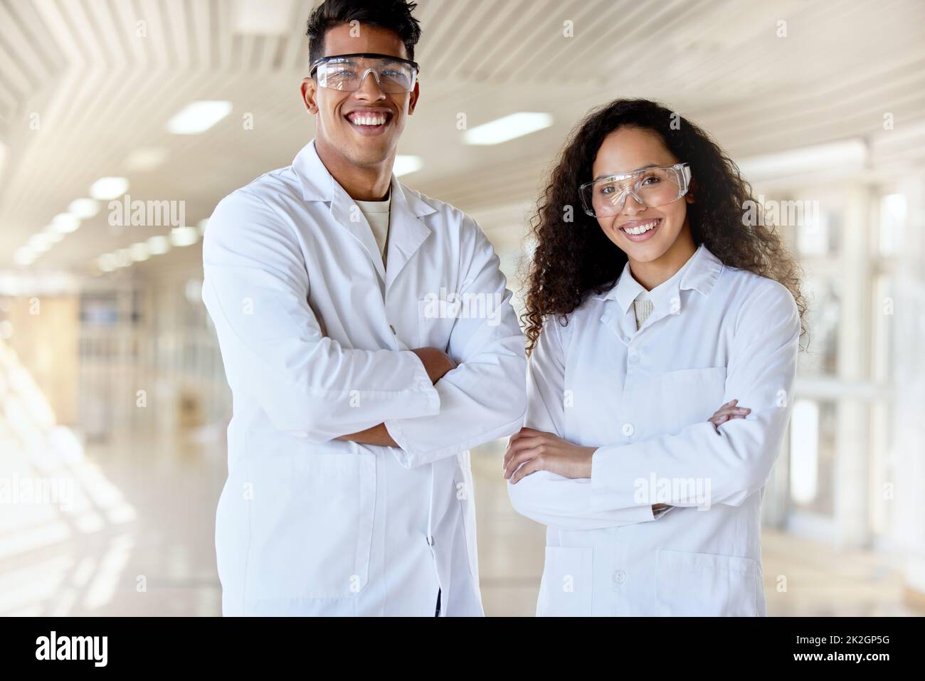 Scientifiques de l'avenir. Portrait court de deux jeunes étudiants en sciences debout avec leurs bras pliés dans un couloir du campus. Banque D'Images