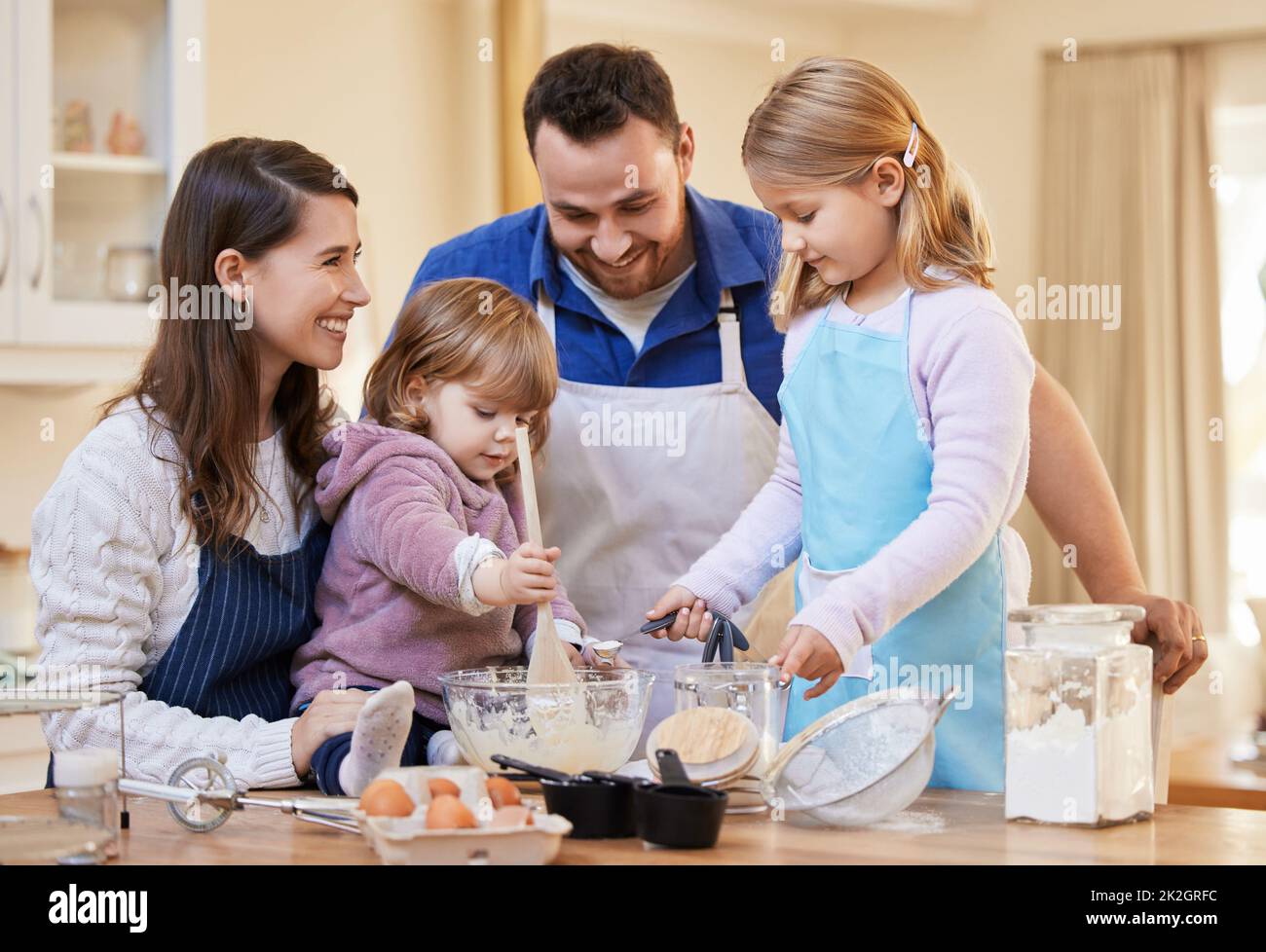 Le temps de la famille est tout ce qui compte. Prise d'une famille qui cuit ensemble tandis qu'une petite fille agite un bol de pâte à gâteau. Banque D'Images